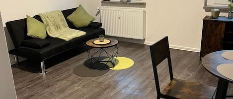 A modern living room with a black sofa, a coffee table, and a dining area with a chair and table.