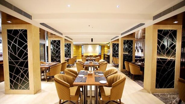 A spacious restaurant with high tables and chairs, featuring geometric patterned walls and a warm color scheme. - FabHotel Prime Bellmont (Noida)