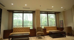 A spacious living room with a large window, a sofa, a chair, and a coffee table. - FabHotel Prime Bellmont (Noida)