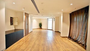 A spacious hallway with wooden flooring, a potted plant, and a large window with curtains. - FabHotel Prime Bellmont (Noida)