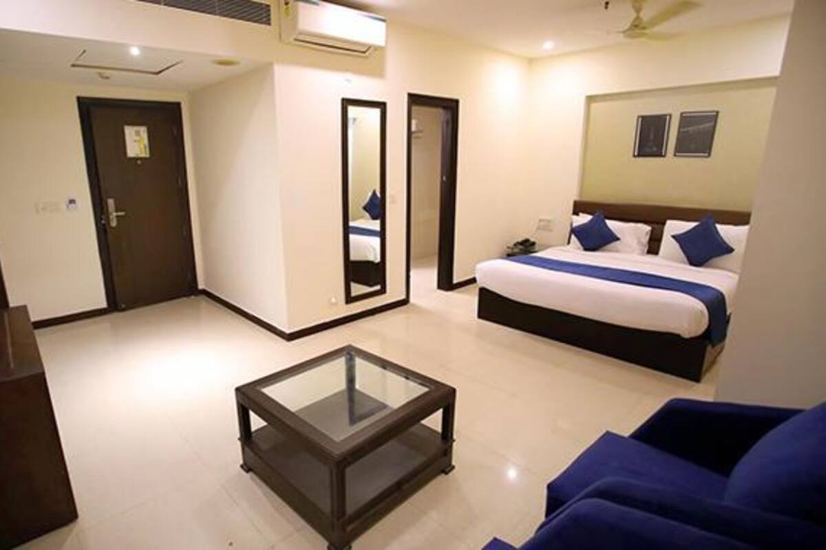 A hotel room with a bed, a glass-top coffee table, a blue sofa, and a door.