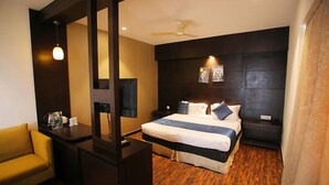 A hotel room with a bed, a desk, a chair, a TV, and a ceiling fan. - FabHotel Prime Bellmont (Noida)