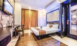 Habitación de hotel con cama, escritorio, silla y televisor.