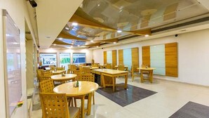 A spacious indoor area with multiple wooden tables and chairs, large windows, and a modern ceiling design. - FabHotel Prime Sukh (Mumbai)
