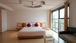 A modern bedroom with a large bed, a nightstand, a glass table, and a window with curtains. - FabHotel Prime Rester Select Chakan (Rajgurunagar)