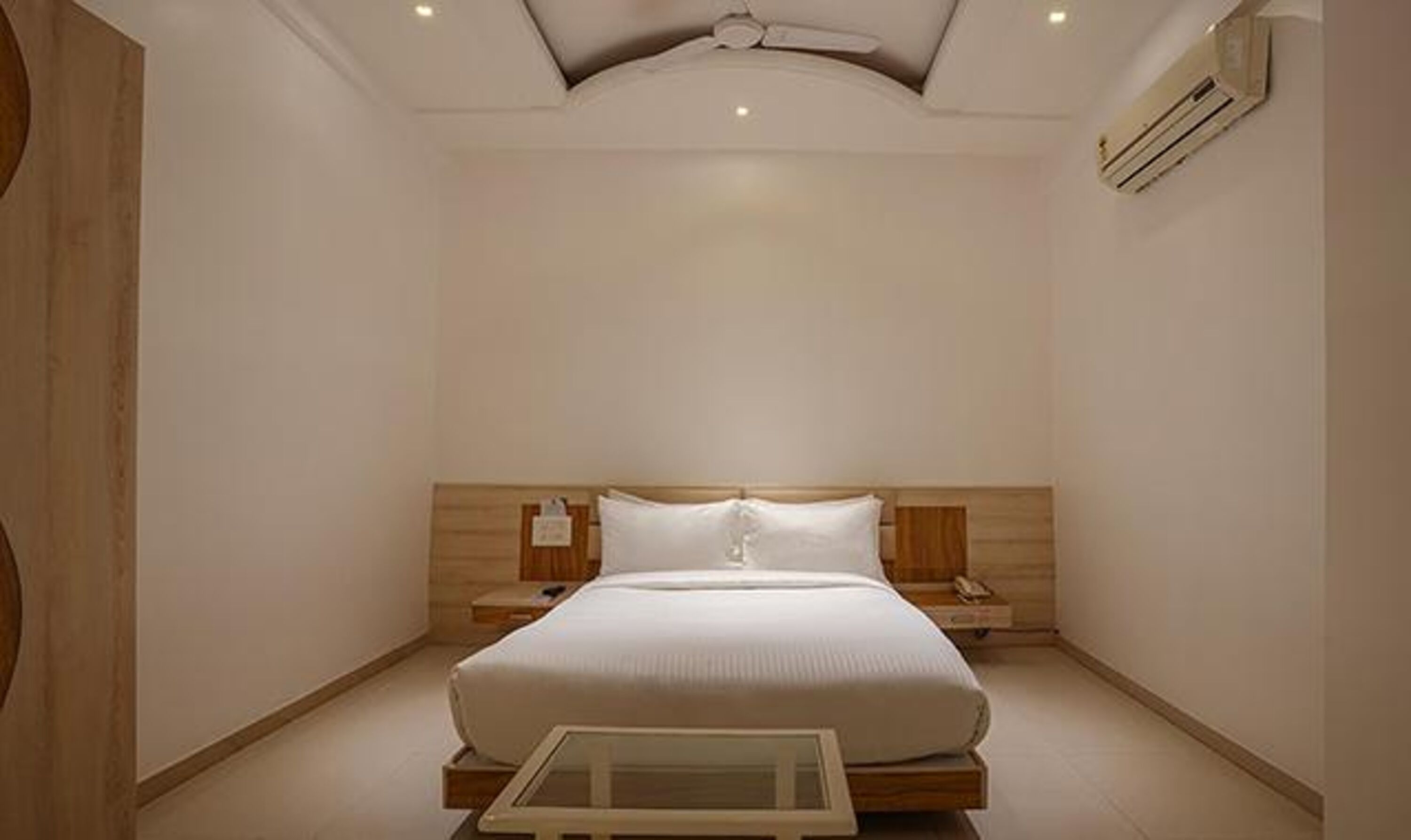 A modern bedroom with a large bed, wooden headboard, bedside tables, and an air conditioning unit.