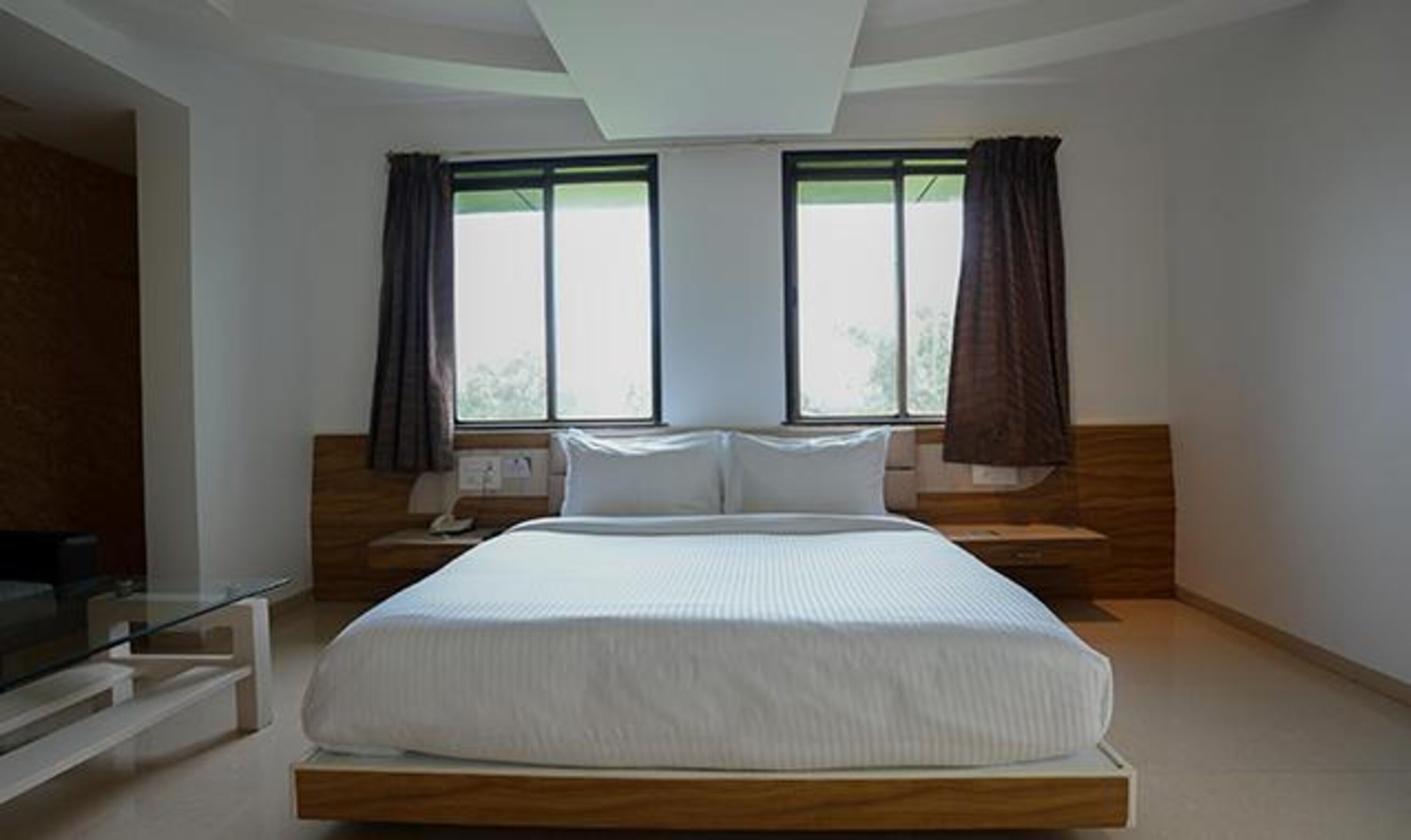 A modern bedroom with a large bed, two bedside tables, a nightstand, and a window with curtains.