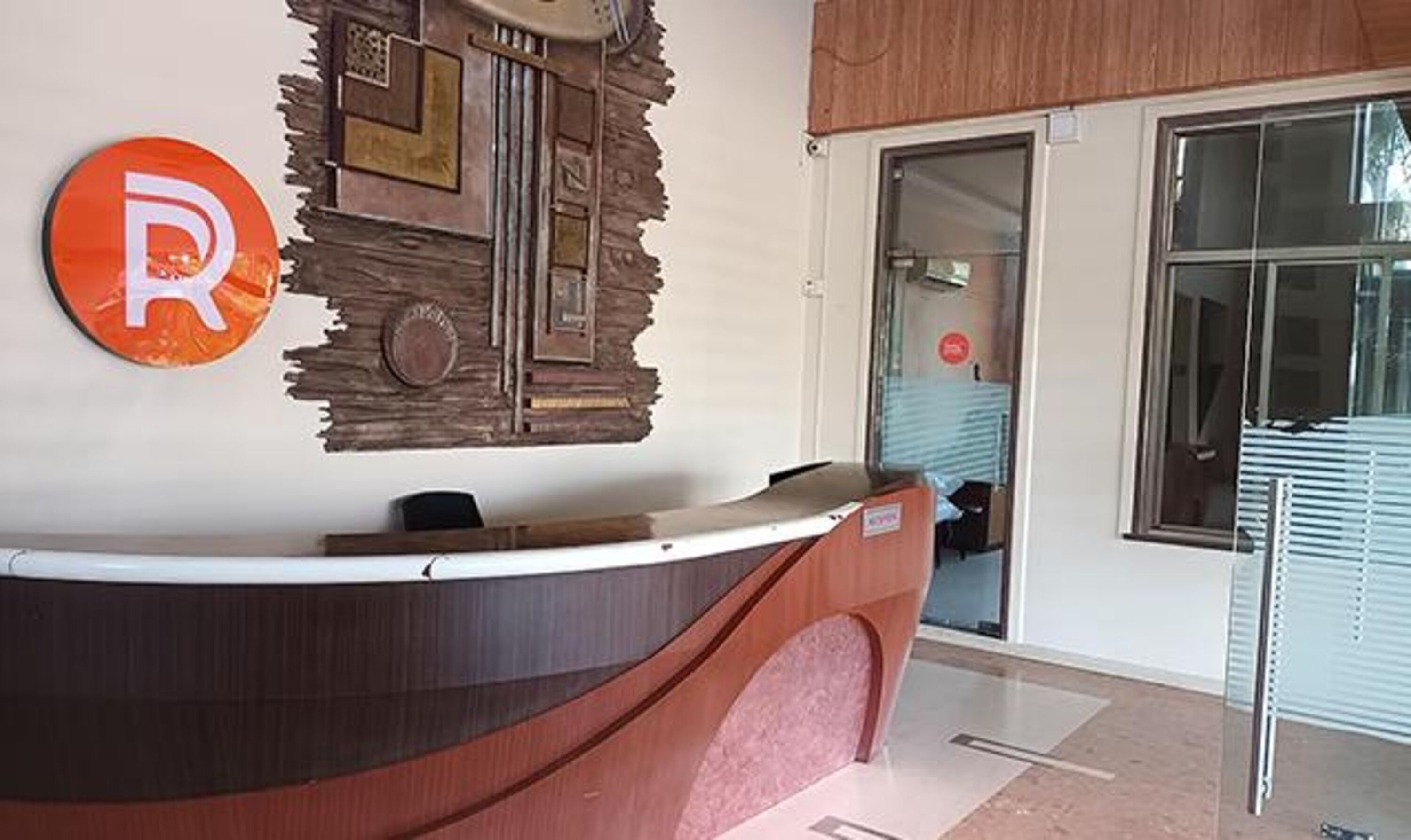 A reception desk with a wooden design, a 'R' logo, and a door leading to a room.