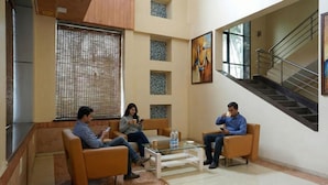 A lobby with three people seated on sofas, a staircase, and a large window with blinds. - FabHotel Prime Rester Select Chakan (Rajgurunagar)