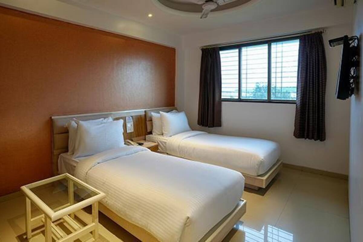 A hotel room with two beds, a small table, and a window with curtains.