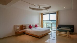 A modern bedroom with a large bed, a nightstand, a sofa, and a ceiling fan. - FabHotel Prime Rester Select Chakan (Rajgurunagar)