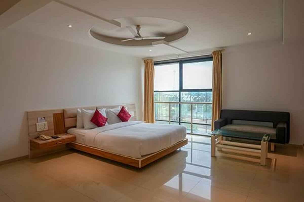 A modern bedroom with a large bed, a nightstand, a sofa, and a ceiling fan.