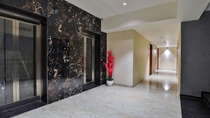 A modern hallway with marble flooring, a glass elevator, and a red flower arrangement. - FabHotel Prime Empyrean (Gandhinagar)