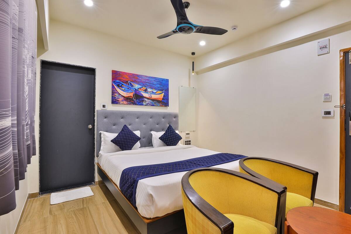 A hotel room with a bed, a ceiling fan, a painting, and a chair.