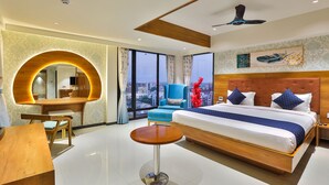 A modern hotel room with a large bed, a desk, a round table, and a view of the city through large windows. - FabHotel Prime Empyrean (Gandhinagar)