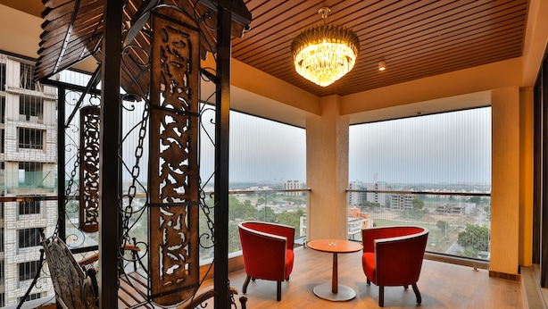A balcony with a wooden floor, two red chairs, a round table, and a chandelier. - FabHotel Prime Empyrean (Gandhinagar)
