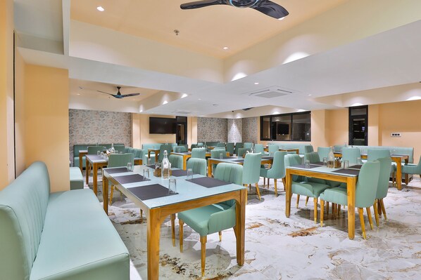 A spacious dining area with multiple tables and chairs, ceiling fans, and a marble floor. - FabHotel Prime Empyrean (Gandhinagar)