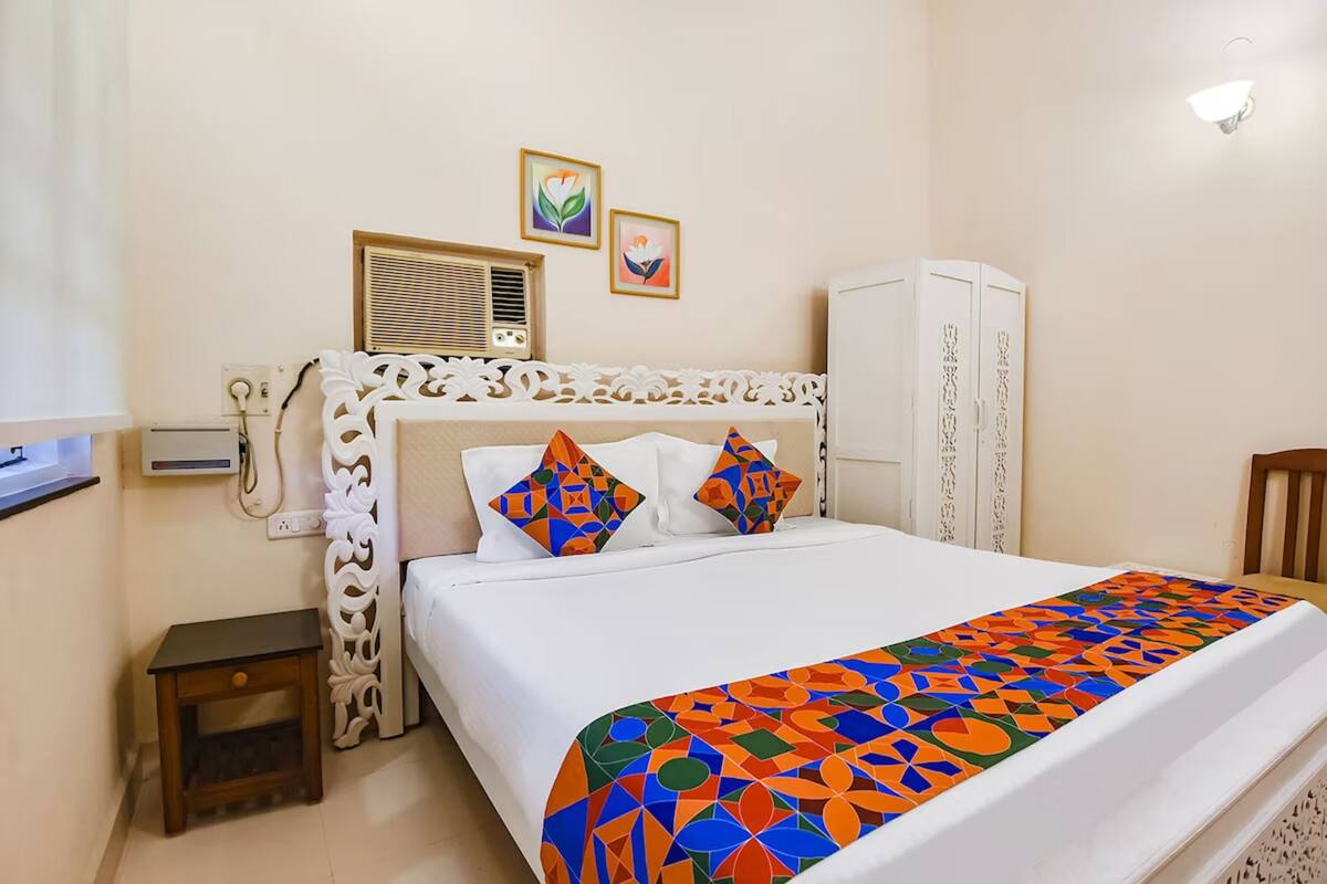A neatly arranged bedroom with a bed, a bedside table, a wardrobe, and a wall-mounted air conditioning unit.