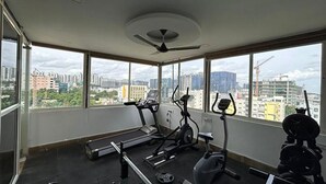 Un gimnasio en un edificio alto con cintas de correr, bicicletas estáticas y un banco para pesas, con amplias ventanas que ofrecen vistas a la ciudad.