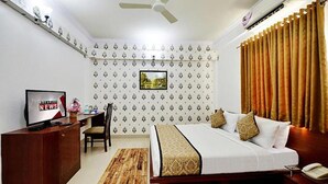 A hotel room with a bed, a desk with a TV, a chair, and a window with curtains. - FabHotel Prime Liverpool Blue (Bengaluru)