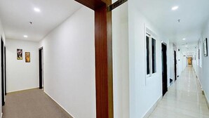A long, narrow hallway with white walls and a wooden column in the center. There are doors on both sides of the hallway, and the floor is carpeted. - FabHotel Prime Liverpool Blue (Bengaluru)