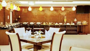 A restaurant with a long counter, multiple tables, and a variety of dishes displayed. - FabHotel Prime Liverpool Blue (Bengaluru)