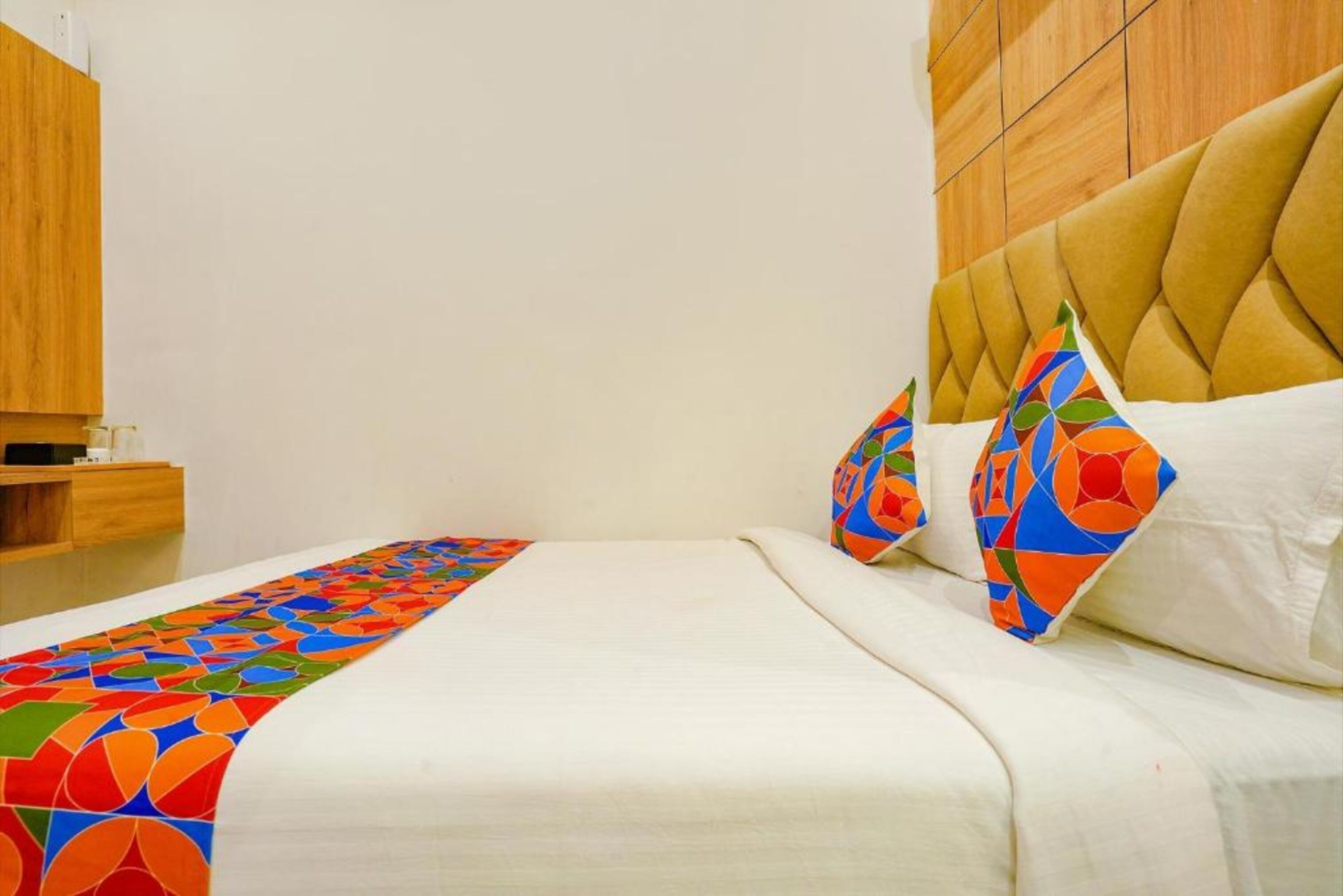 A neatly made bed with a colorful geometric-patterned bed runner, a tufted headboard, and two pillows with a similar geometric design.