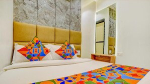 Quarto de hotel com cama, duas almofadas estampadas com padrões geométricos, parede de mármore, mesa de cabeceira de madeira e um espelho.