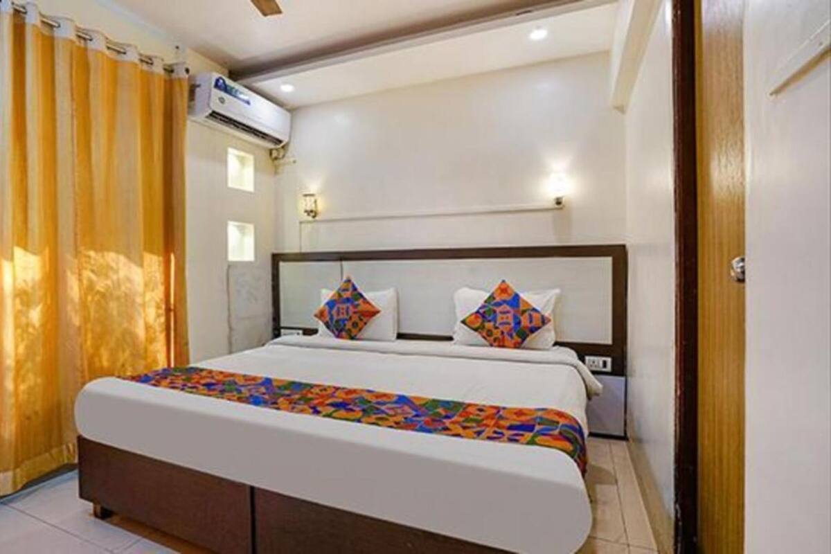 A hotel room with a bed, curtains, an air conditioning unit, and a wall-mounted light fixture.