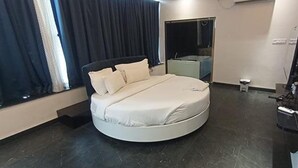 A circular bed in a modern room with a dark floor, a small bedside table, and a television on the right. - FabHotel Prime Kanha Shree (Indore)