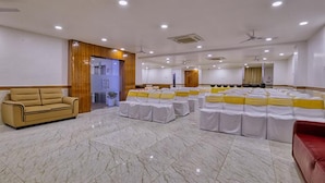 A spacious conference room with a marble floor, rows of tables with white and yellow sashes, a beige sofa, and a wooden accent wall. - FabHotel Ten Eleven Grand (Indore)