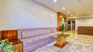 A reception area with a wooden reception desk, a cushioned bench, a glass-top table, and a potted plant. - FabHotel Ten Eleven Grand (Indore)