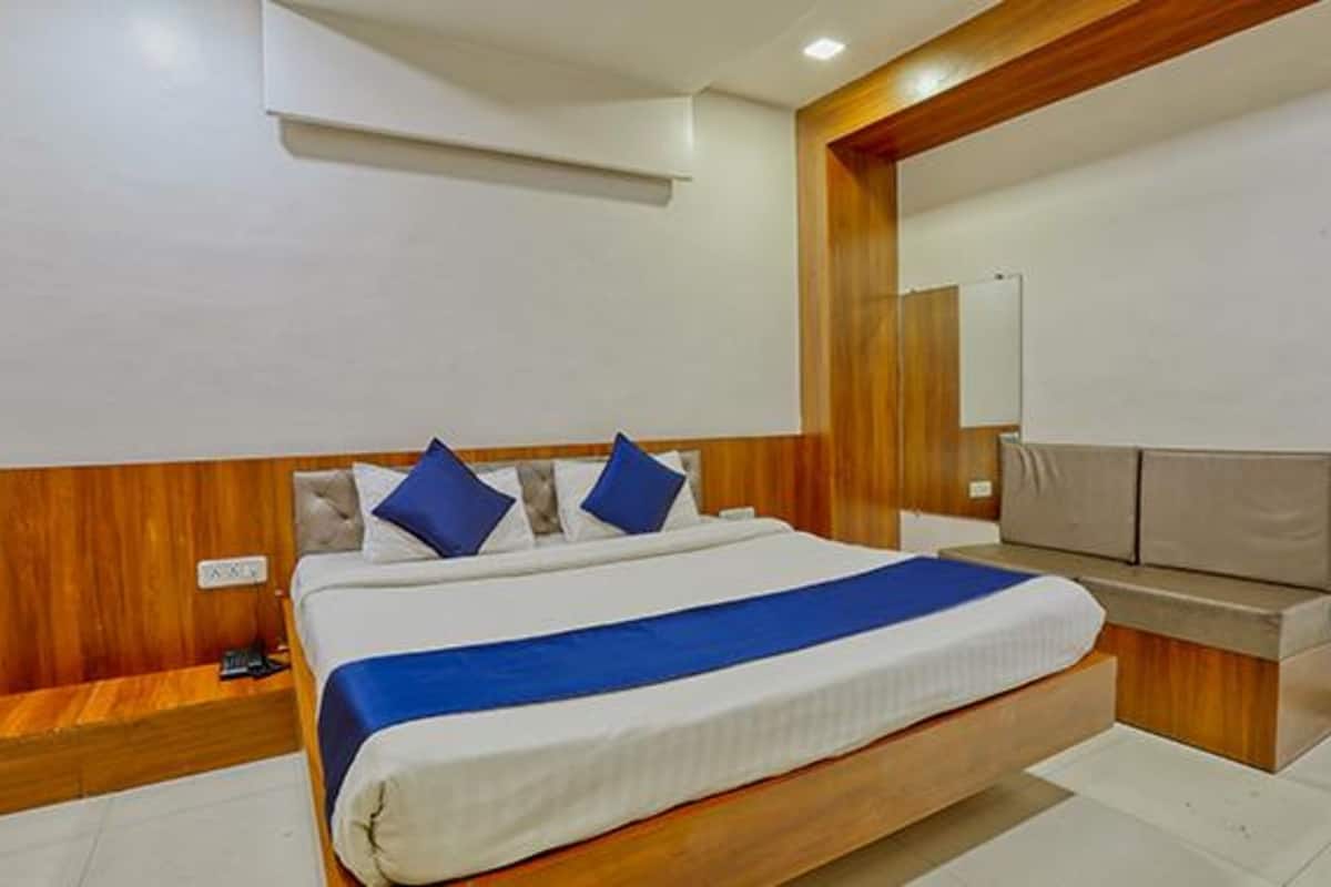 A modern hotel room with a large bed, wooden headboard, and a built-in bench at the foot of the bed.