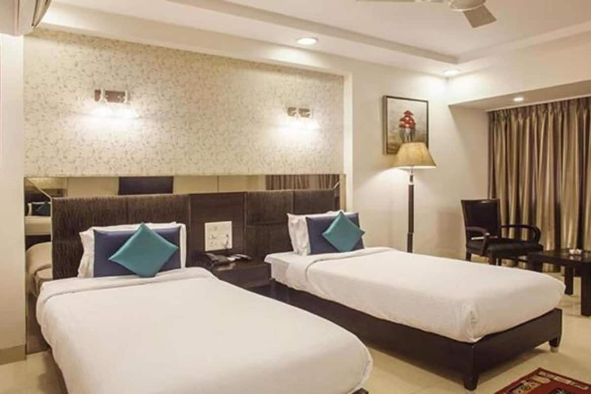Habitación de hotel con dos camas individuales, un escritorio, una silla, una lámpara y un cuadro en la pared.