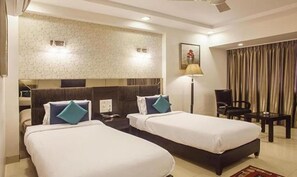 A hotel room with two single beds, a desk, a chair, a lamp, and a painting on the wall. - FabHotel Prime Hema's Supreme (Visakhapatnam)