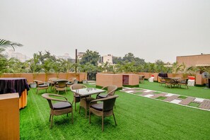 An outdoor seating area with wicker chairs and tables, surrounded by artificial grass and potted plants. - Fabhotel Prime The Rivlet Mg Road (Gurugram)