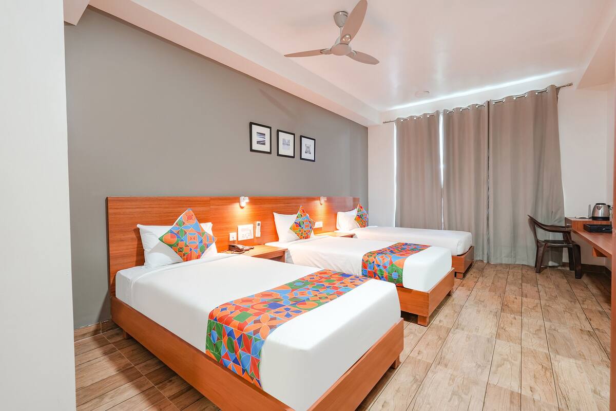 A hotel room with two beds, a desk, a chair, a ceiling fan, and a window with curtains.