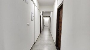 A long, narrow hallway with white walls and a grey floor, leading to a door at the end. - FabHotel KSP Kings Inn (Bengaluru)
