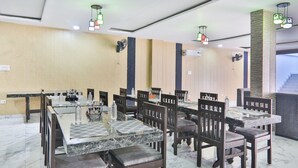 A hotel dining area with marble tables, wooden chairs, and green hanging lights. - FabHotel Lucknow Inn (Lucknow)