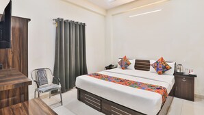 A hotel room with a bed, bedside table, chair, and a TV mounted on the wall. - FabHotel Lucknow Inn (Lucknow)