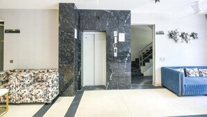 A lobby with a marble reception desk, a sofa, a blue sofa, and a staircase. - FabHotel Prime Y Stay (Greater Noida)
