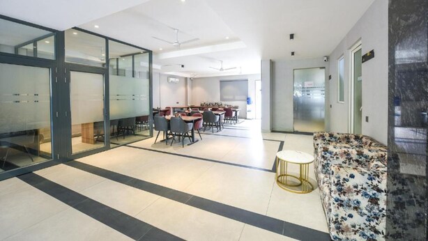 A modern interior with a dining area, glass partitions, and a sofa. - FabHotel Prime Y Stay (Greater Noida)