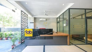 A hotel reception area with a modern design, including a reception desk, glass walls, and potted plants. - FabHotel Prime Y Stay (Greater Noida)