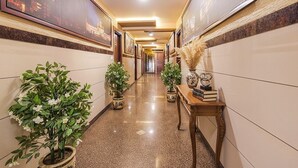 A hotel hallway with framed artwork on the walls, potted plants, and a wooden table with books and decorative items. - FabHotel Ginger Suites (Bengaluru)