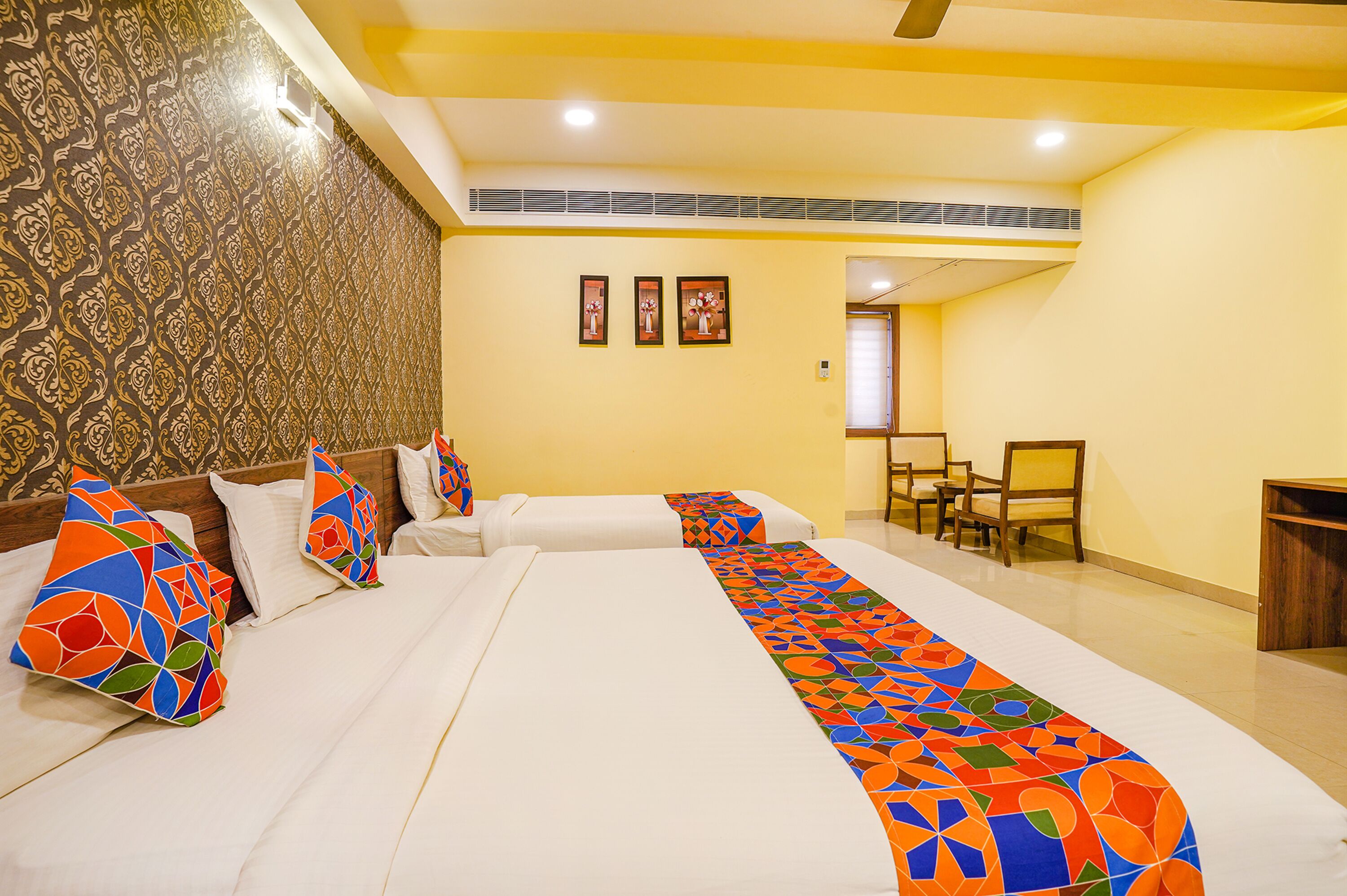 A hotel room with a large bed, two pillows, a patterned wall, and a small table with chairs.