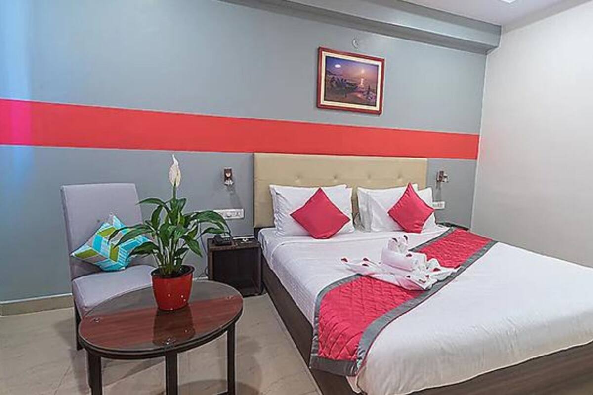A hotel room with a bed, a chair, a small table, and a potted plant.