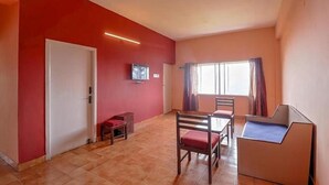 A room with a red wall, a white door, a small table with a chair, a bed, and a window with curtains. - FabHotel Green Castle Resort (Kodaikanal)