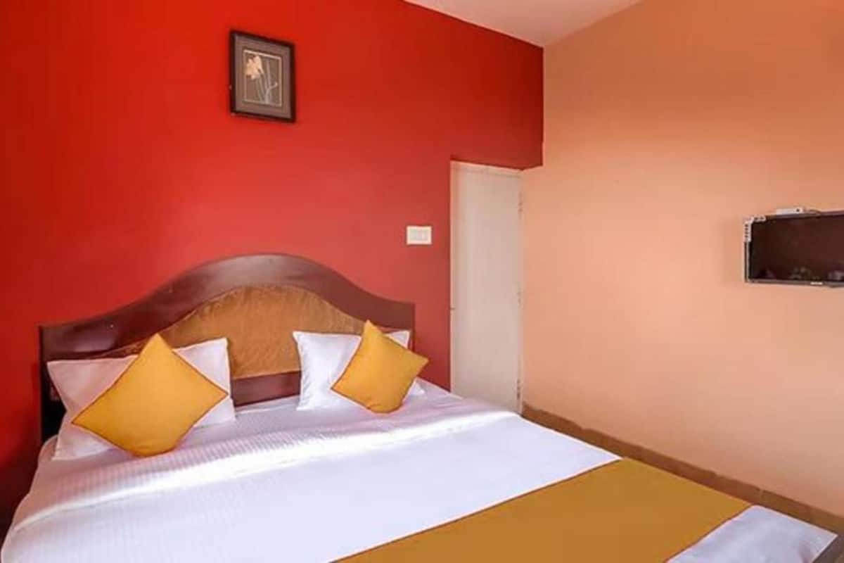 A hotel room with a bed, a wooden headboard, and a red wall.