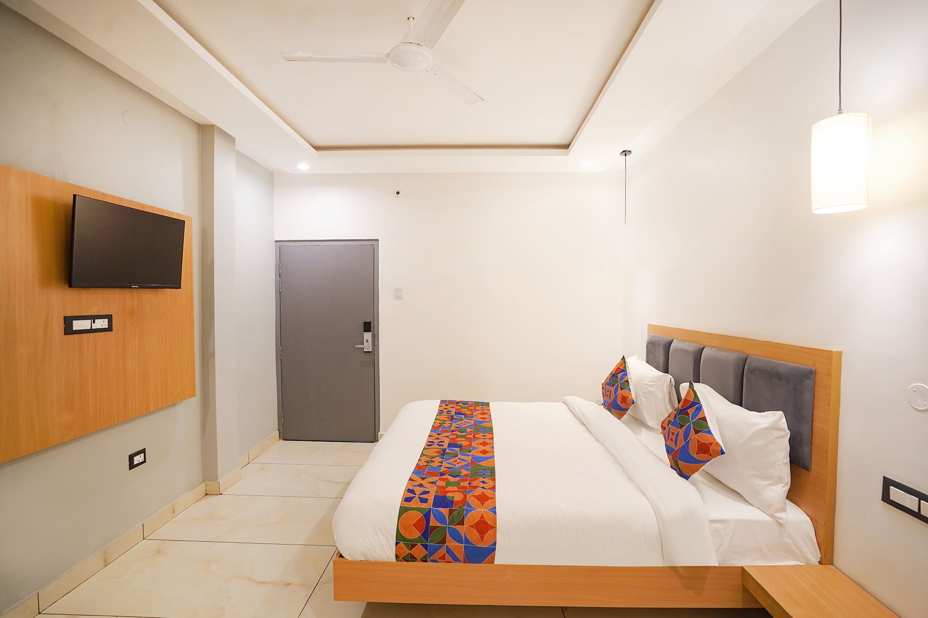 A hotel room with a bed, a television mounted on the wall, a door, and a ceiling fan.