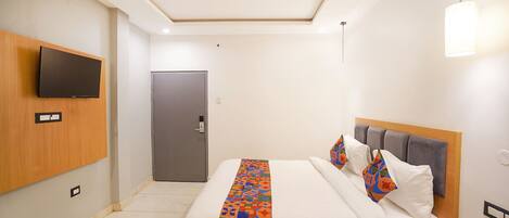 A hotel room with a bed, a television mounted on the wall, a door, and a ceiling fan.